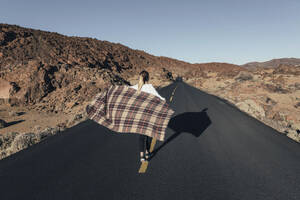 Junge Frau geht mit Decke in der Nähe von Vulkanlandschaft an einem sonnigen Tag - MMPF00985