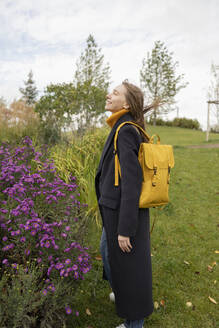 Frau mit Rucksack steht in der Nähe von Pflanzen im Park - LESF00498