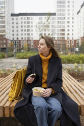Junge Frau sitzt auf einer Bank und isst zu Mittag im Park - LESF00500