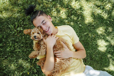 Lächelnder Mann mit Hund im Arm und im Gras liegend im Park - NLAF00161