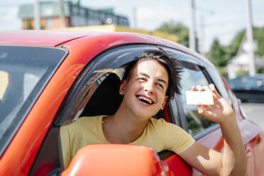 Smiling man showing driver's license and leaning out of car window - NLAF00180