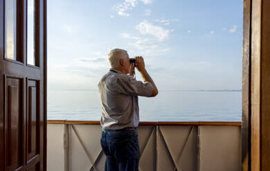 Mann schaut vom Schiff aus durch ein Fernglas aufs Meer - MBLF00071