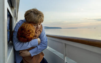 Liebevolle ältere Frau, die ihren Enkel auf einem Schiff in der Abenddämmerung umarmt - MBLF00074