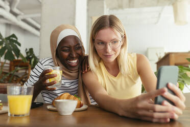 Smiling friends taking selfie with food on table at coffee shop - EBSF04002