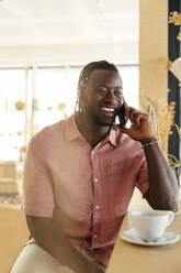 Smiling man talking on smart phone in coffee shop - EBSF04016