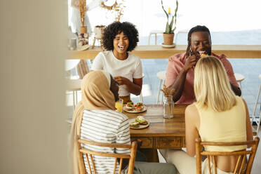 Smiling friends having bruschettas and orange juice at table in coffee shop - EBSF04017