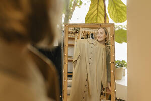 Lächelnde Frau beim Anprobieren eines Kleides und beim Betrachten des Spiegels im Geschäft - VIVF01119