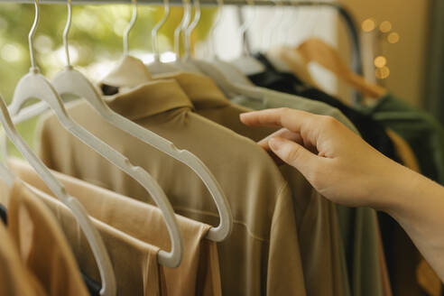 Woman choosing dress from clothes rack in store - VIVF01125