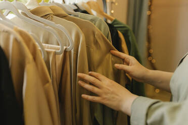 Hände einer Frau, die ein Kleid von einem Kleiderständer in einem Geschäft auswählt - VIVF01126