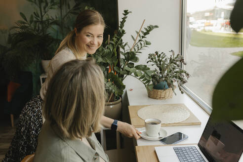 Smiling waiter serving coffee to freelancer in coffee shop - VIVF01140