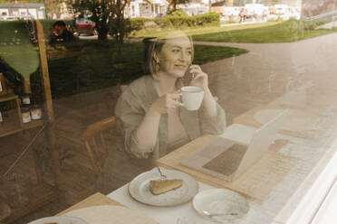 Lächelnder Freiberufler, der eine Kaffeetasse hält und mit seinem Smartphone in einem Café spricht - VIVF01142