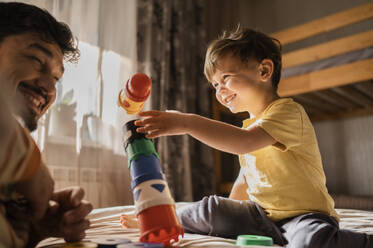 Cheerful boy and father playing with toy blocks at home - ANAF02338