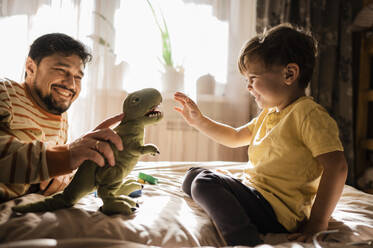 Father and son playing with stuffed toy at home - ANAF02340
