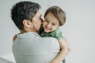 Happy man embracing son in front of white wall - ANAF02353