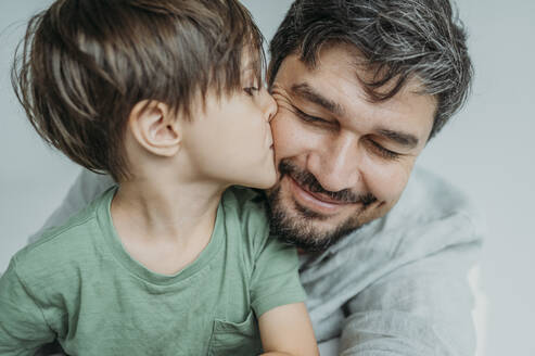 Son kissing father on cheek against white background - ANAF02368