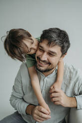 Son kissing smiling father against white background - ANAF02369
