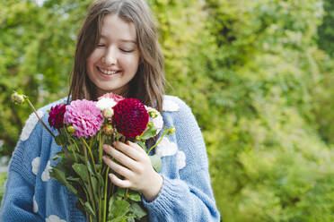 Happy girl holding dahlia flowers in front of plants - IHF01775