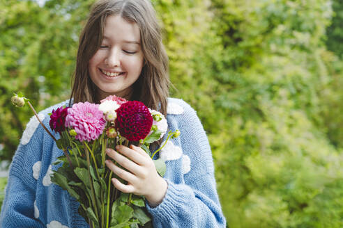 Glückliches Mädchen hält Dahlienblüten vor Pflanzen - IHF01775