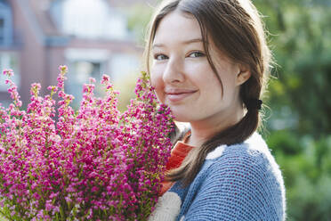 Smiling girl holding heather flowers on sunny day - IHF01777