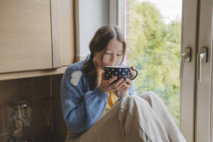 Girl drinking hot chocolate near window at home - IHF01790