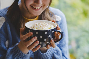 Happy girl holding mug of hot chocolate with whipped cream - IHF01794
