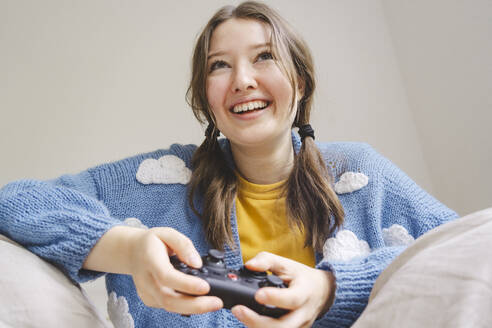 Happy girl playing video game with controller at home - IHF01808
