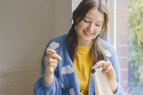 Smiling teenage girl sewing button on clothing - IHF01810