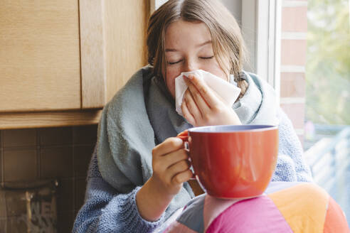 Teenager-Mädchen hält große Kaffeetasse und putzt Nase mit Taschentuch zu Hause - IHF01818