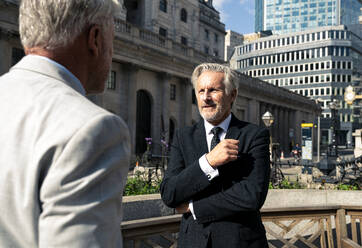 Smiling senior businessman having discussion with colleague in front of buildings - OIPF03576