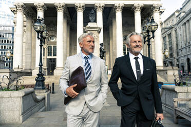 Ein lächelnder Geschäftsmann steht mit einem Kollegen vor einem Finanzgebäude - OIPF03581