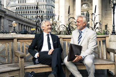 Happy senior businessmen having discussion together on bench in front of buildings - OIPF03583
