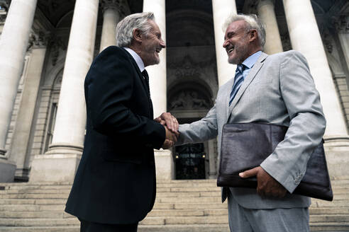 Happy senior businessman holding hands with colleague in front of building - OIPF03589