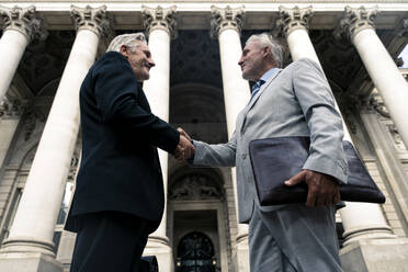 Lächelnder Geschäftsmann beim Händeschütteln mit einem Kollegen in der Nähe eines Gebäudes - OIPF03590