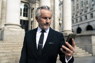Ein älterer Geschäftsmann benutzt ein Smartphone in der Nähe eines Gebäudes - OIPF03598