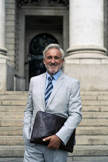 Glücklicher älterer Geschäftsmann mit Tasche vor einer Treppe stehend - OIPF03601