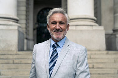 Lächelnder älterer Geschäftsmann mit grauem Haar vor einem Gebäude - OIPF03602