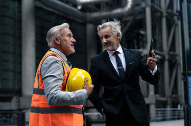 Smiling senior businessmen holding hardhat and tablet PC on street - OIPF03628