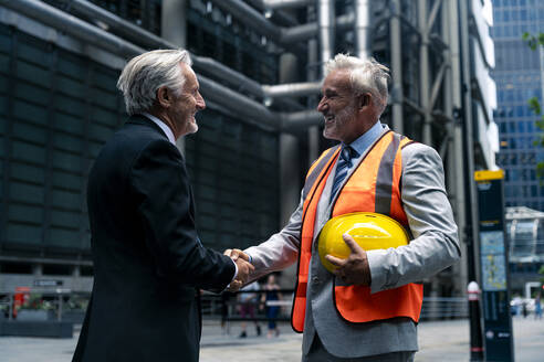 Senior businessman holding hardhat and shaking hands with colleague - OIPF03631