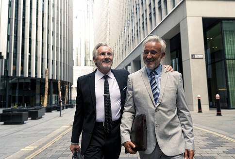 Happy senior businessmen walking and talking with each other amidst financial buildings - OIPF03634