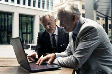 Älterer Geschäftsmann diskutiert mit einem Kollegen über einem Laptop am Tisch - OIPF03640