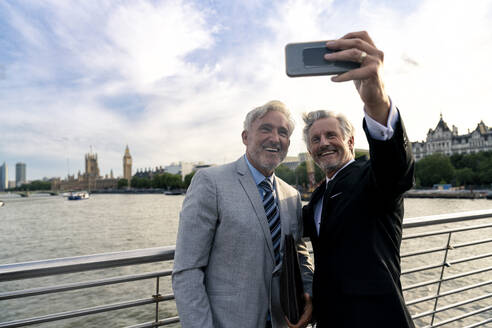 Happy senior businessman taking selfie in front of Thames river - OIPF03651