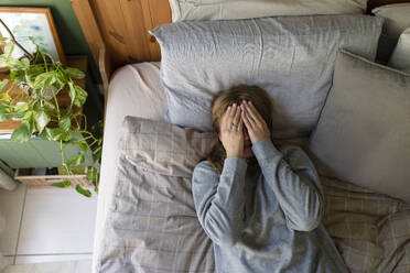 Gestresste Frau mit Händen, die das Gesicht bedecken, liegt zu Hause auf dem Bett - SVKF01683