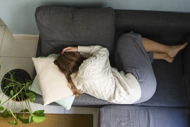 Woman with stomach cramp sleeping on sofa at home - SVKF01695