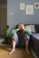 Stressed woman covering face sitting on carpet at home - SVKF01699