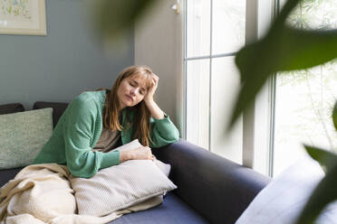 Sad woman with head in hands sitting on sofa at home - SVKF01700