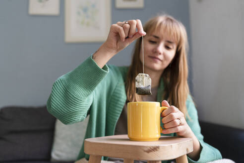 Smiling woman dipping teabag in mug at home - SVKF01701