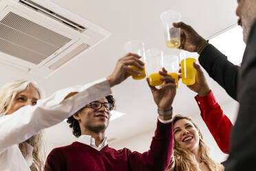 Smiling coworkers toasting juice glasses at work place - PBTF00370