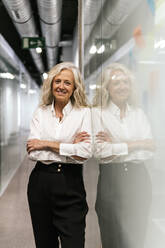 Smiling mature businesswoman with arms crossed at work place - PBTF00388