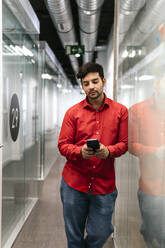 Junger Geschäftsmann benutzt sein Smartphone im Korridor am Arbeitsplatz - PBTF00390
