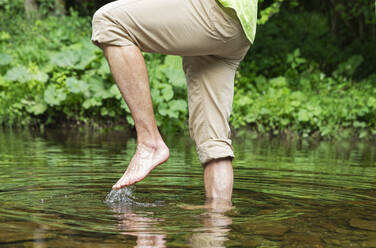 Senior man walking barefoot in river - GWF07930